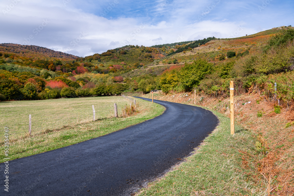 Road curves through green fields towards mountains in autumn colors in the French Pyrenees