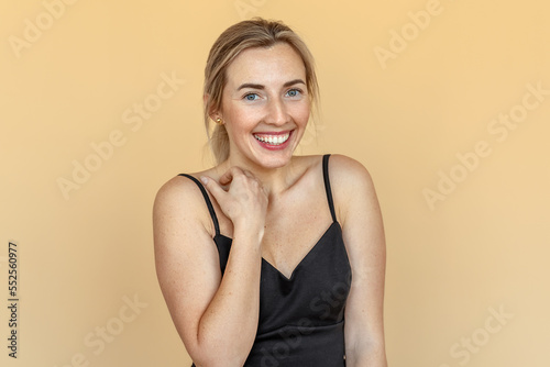Shy, timid, pretty young woman with freckles stands over beige background. Beautiful girl surprised and wondered looks on you. Expressive facial expressions