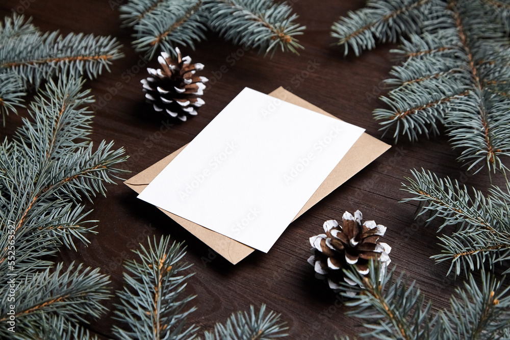 Christmas card mockup with envelope, green fir tree branches and cones on brown wooden background. Blank holiday card with winter decoration Christmas card mockup with envelope, green fir tree branches and cones on brown wooden background. Blank holiday card with winter decoration