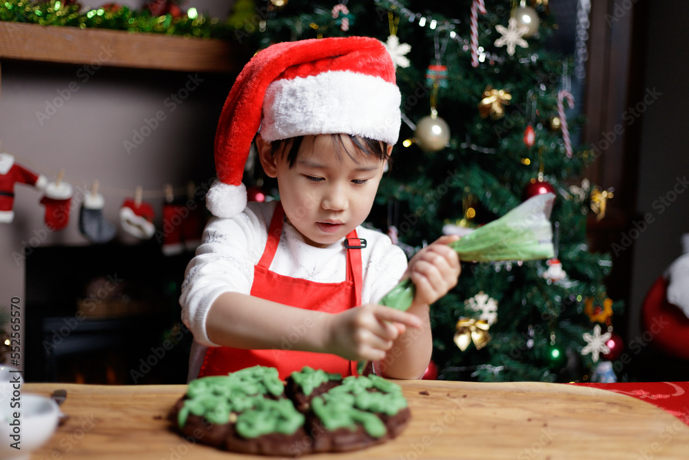 young girl wearing Santa hat was preparing cake for Christmas party in front of Christmas tree at home young girl wearing Santa hat was preparing cake for Christmas party in front of Christmas tree at home