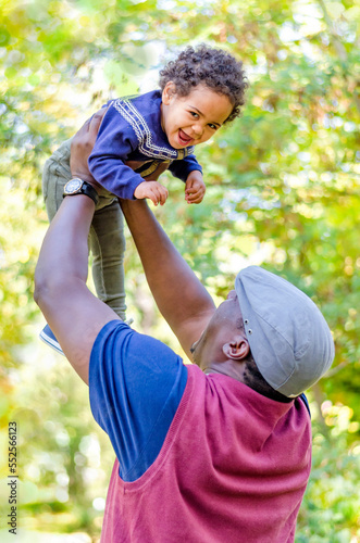 Happy funny african american kid girl flying in fathers arms looking at camera outdoors, loving family devoted dad holding lifting cute little child daughter