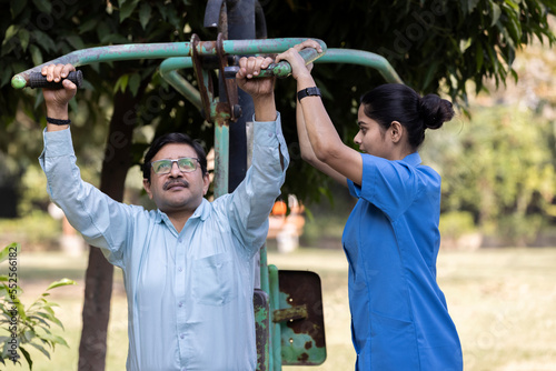 Photography A physiotherapist or professional caregiver watches closely as a senior adult woman exercises on an outdoor gym