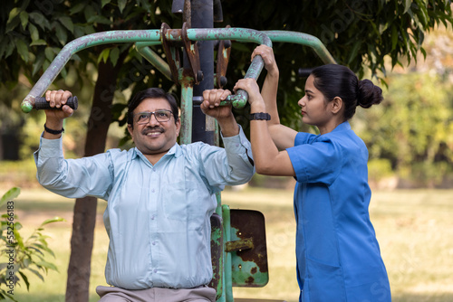 Photography A physiotherapist or professional caregiver watches closely as a senior adult woman exercises on an outdoor gym