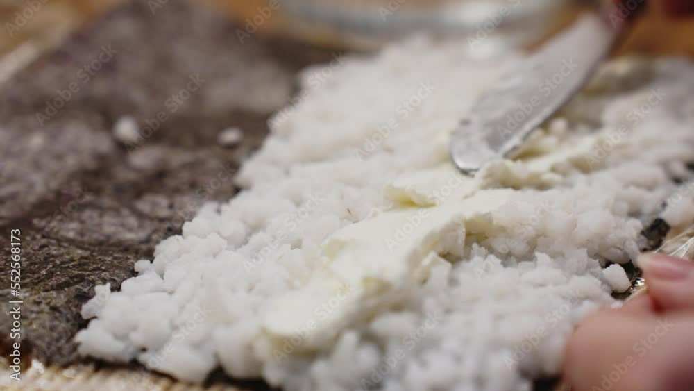 Closeup detail of knife spreading cheese on top of rice, sushi roll