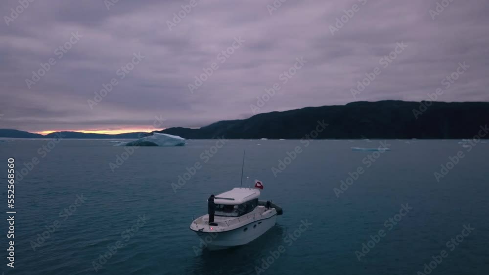 Aerial of a motorboat in ice water by a giant icecap. Beautiful sunset, panning left. Aerial of a motorboat in ice water by a giant icecap. Beautiful sunset, panning left.