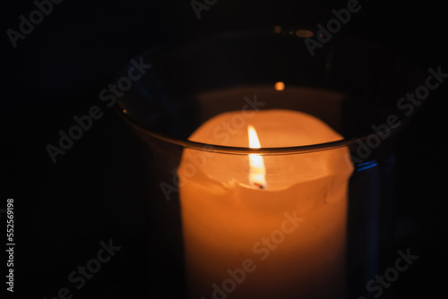 A candle in glass candlestick glows in a dark, close up photo