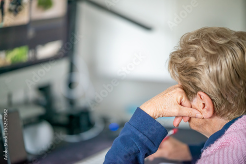 Woman working with a desktop computer at home, taking notes with a pen