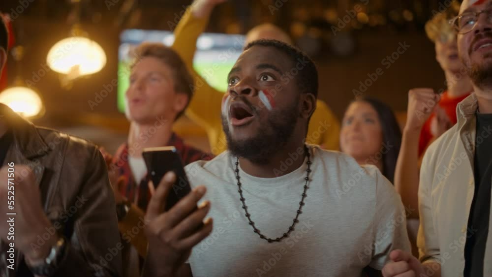 Portrait of an Excited Young Black Man Holding a Smartphone, Anxious About a Sports Bet on His Favorite Soccer Team. Lively Successful Emotions When Football Team Scores a Winning Goal.