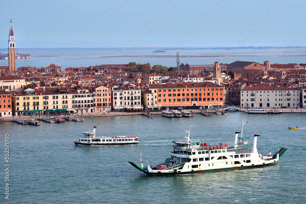 Cityscape, bird view of Venice Castello region and sea lagoon with vaporetto terminals and ferry boat in foreground. Toned panoramic image in orange and blue colors.