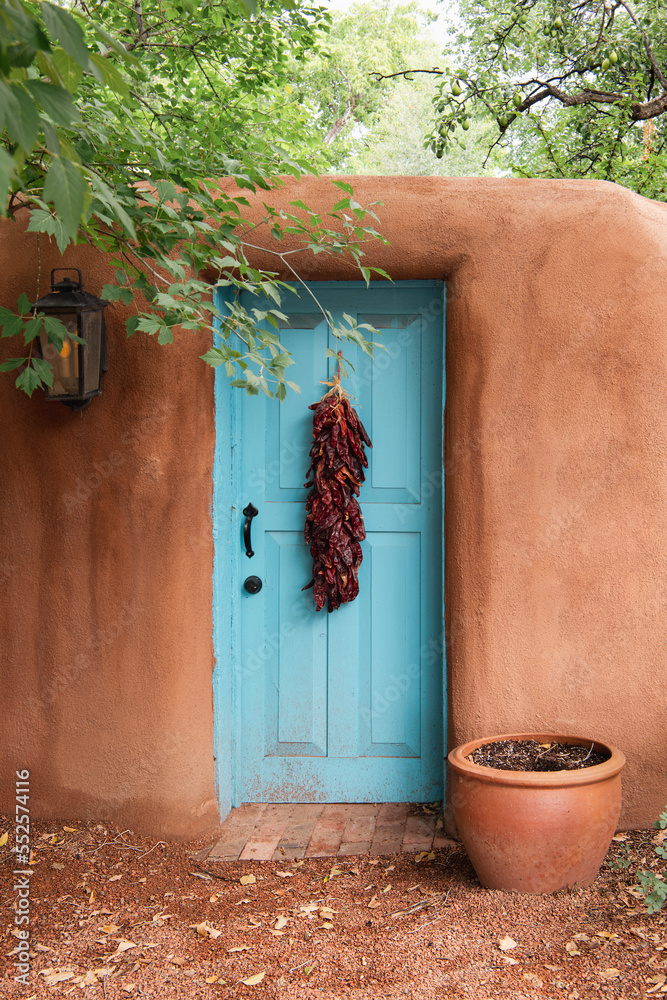 Fototapeta premium Turquoise door with chile ristra in adobe wall in Santa Fe, New Mexico