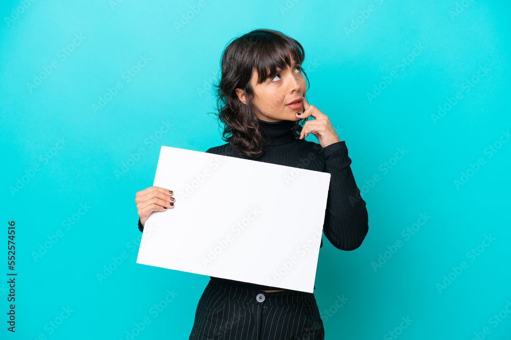 Young latin woman isolated on blue background holding an empty placard and thinking Young latin woman isolated on blue background holding an empty placard and thinking
