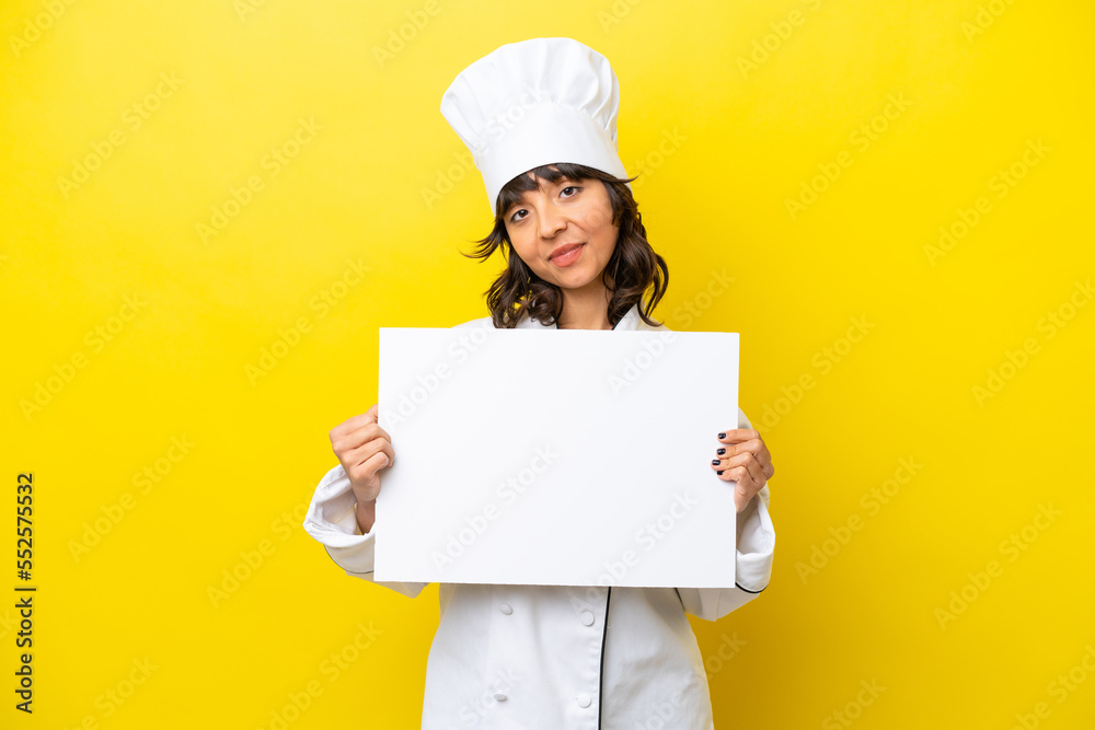Young chef latin woman isolated on yellow background holding an empty placard with happy expression Young chef latin woman isolated on yellow background holding an empty placard with happy expression