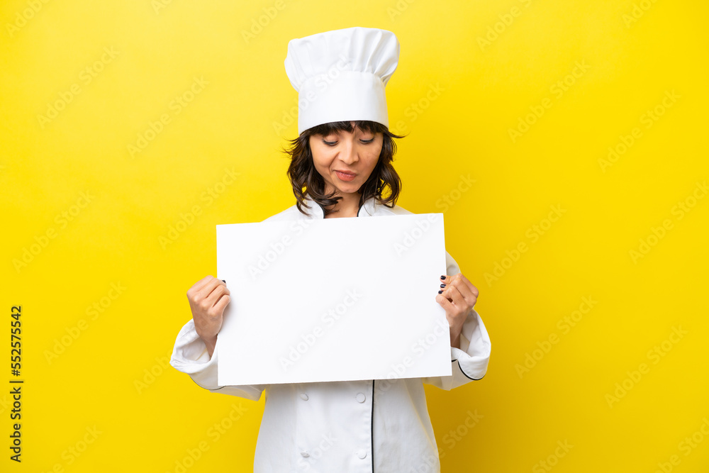 Young chef latin woman isolated on yellow background holding an empty placard and looking it Young chef latin woman isolated on yellow background holding an empty placard and looking it