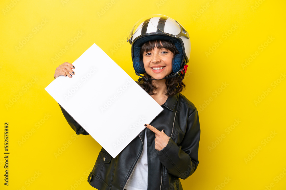 Young latin woman with a motorcycle helmet isolated on yellow background holding an empty placard with happy expression and pointing it Young latin woman with a motorcycle helmet isolated on yellow background holding an empty placard with happy expression and pointing it
