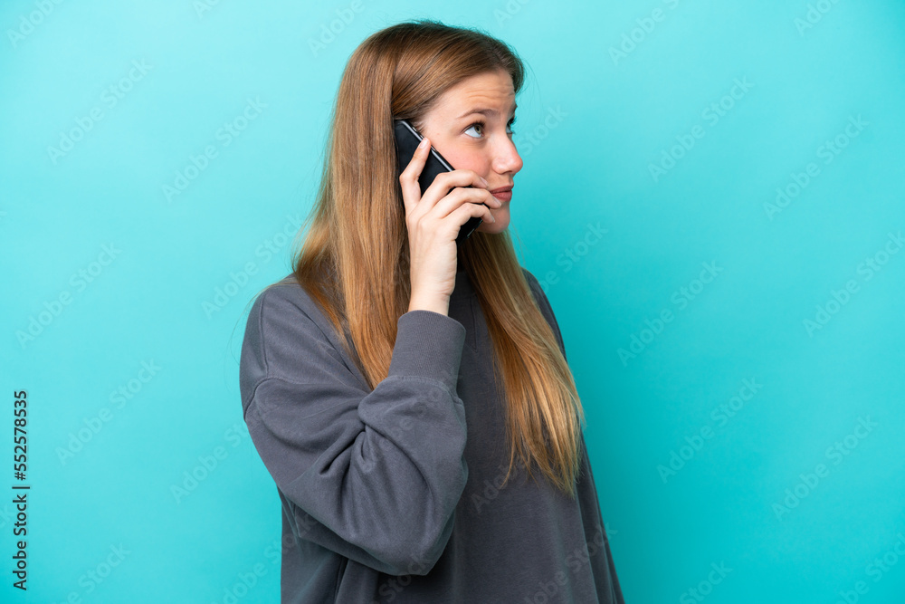 Young caucasian woman isolated on blue background keeping a conversation with the mobile phone with someone