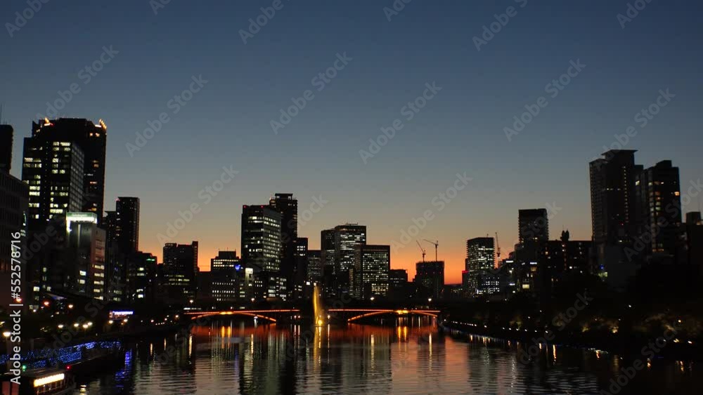 OSAKA, JAPAN - SEP 2022 : Office buildings at Kitahama area and river in sunset. Large business district in Osaka. Time lapse shot, dusk to night. Japanese business, company and urban city concept.