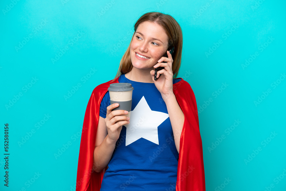 Super Hero caucasian woman isolated on blue background holding coffee to take away and a mobile Super Hero caucasian woman isolated on blue background holding coffee to take away and a mobile