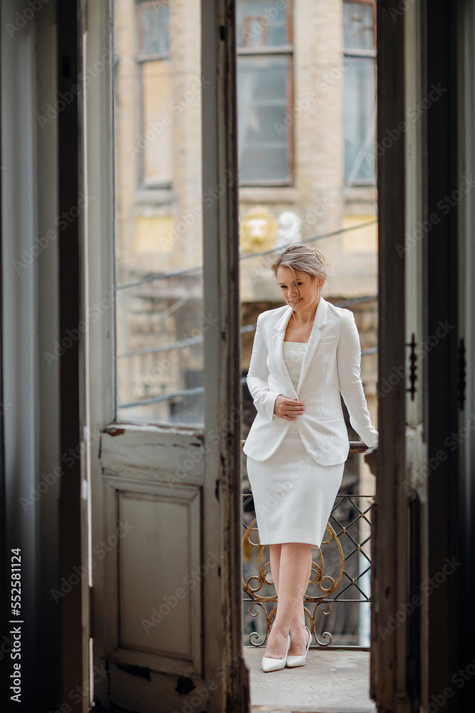 a beautiful, confident woman in a white suit on the balcony of the old building.