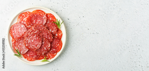 Sliced salami sausage on a plate over white background with space for text