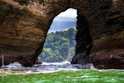 natural bridge in the rocks on the pacific coast of costa rica in marino ballena national park; view through a tunnel in the rocks to a paradise beach with palm trees