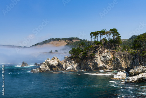 Rugged coastal cliffs and rock formations above the sea and fog at Point Lobos State Preserve, Carmel, California