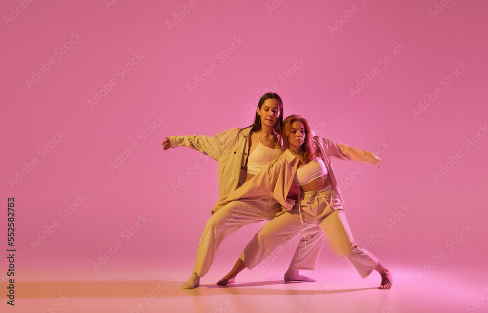Two stylish female dancers in casual style clothes dancing contemporary choreography dance over crystal pink background. Concept of modern art, creativity, fusion Two stylish female dancers in casual style clothes dancing contemporary choreography dance over crystal pink background. Concept of modern art, creativity, fusion