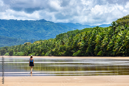a lone beautiful girl in a skirt walks along a tropical beach with palm trees in marino ballena national park in costa rica; relaxing on a paradise beach in costa rica