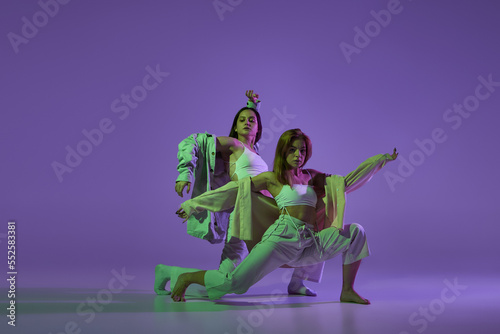 Dance performance. Stylish female dancers at contemporary choreography dance class isolated over crystal purple background. Style  youth  music and fashion