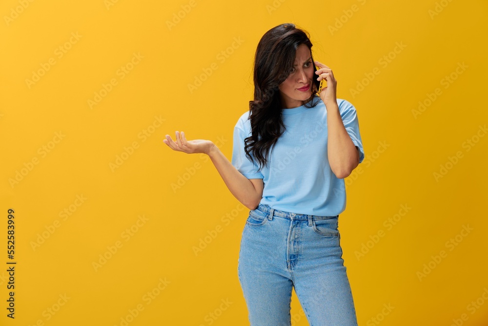 Woman blogger with a phone in her hands in a blue t-shirt and jeans on a  yellow background smile signs gestures symbols, online communication and  video call, copy space, free background Stock