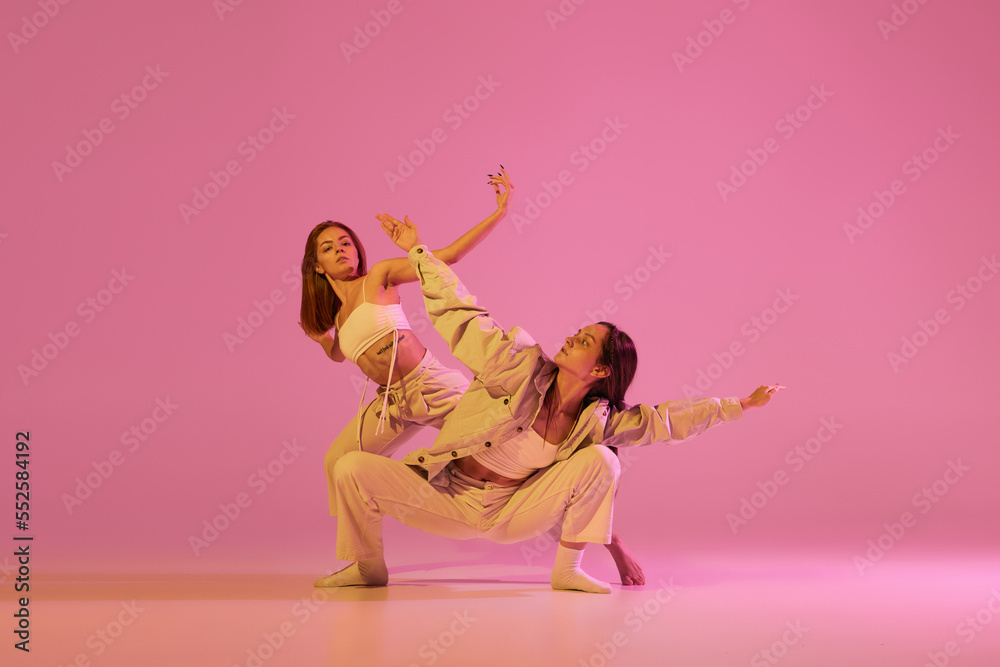 Obraz premium Two stylish female dancers in casual style clothes dancing contemporary choreography dance over crystal pink background. Concept of modern art, creativity, fusion