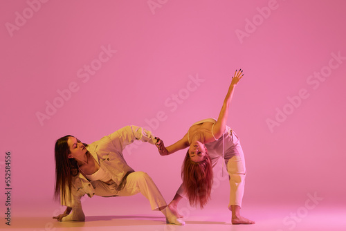 Two stylish female dancers in casual style clothes dancing contemporary choreography dance over crystal pink background. Concept of modern art, creativity, fusion