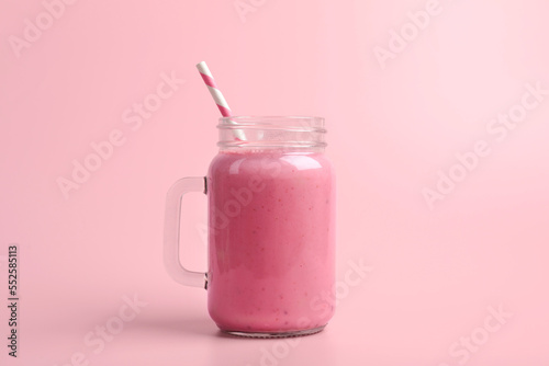 Mason jar with delicious berry smoothie on pink background