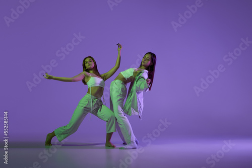 Fototapeta Naklejka Na Ścianę i Meble -  Studio footage of dancing young girls. Stylish performance. Two young women in expressive contemporary dance isolated over purple background.