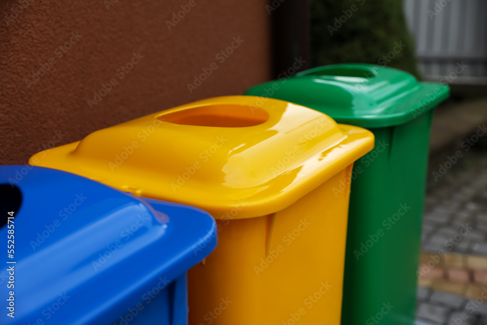 Many color recycling bins near brown wall outdoors, closeup