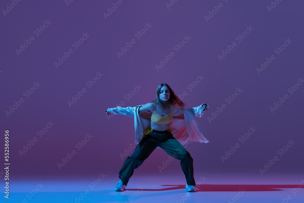 Flexible young girl, contemp dancer dancing hip-hop or experimental dance isolated on dark purple background in neon. Contemporary dance. Music, dance, active lifestyle, fashion, style