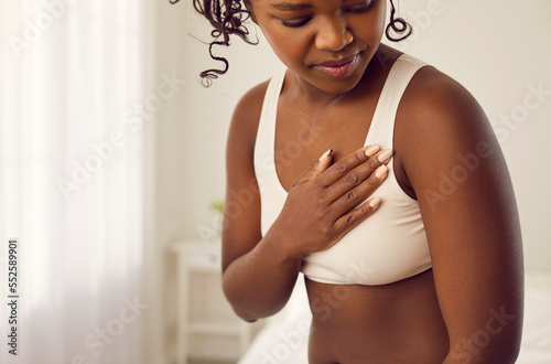 Beautiful young black woman in underwear suddenly feels pangs of pain and touches her chest. Heart attack, infarct, cardiac disease, mastitis, breast cancer symptoms concept