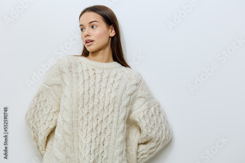 an attractive, young woman is standing in a white stylish sweater on a light background looking pleasantly to the side with well-groomed, straight hair