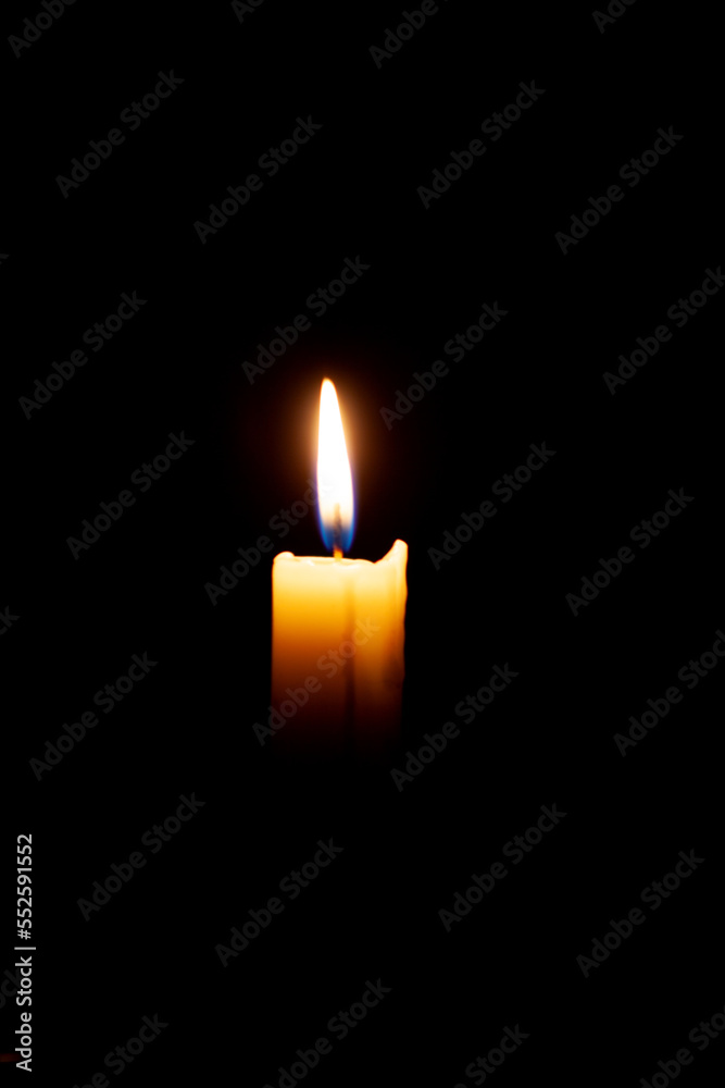 A burning candle on a black background in a dark room. A burning candle on a black background in a dark room.