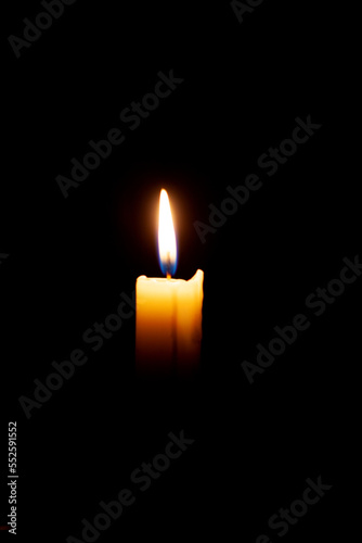 A burning candle on a black background in a dark room.