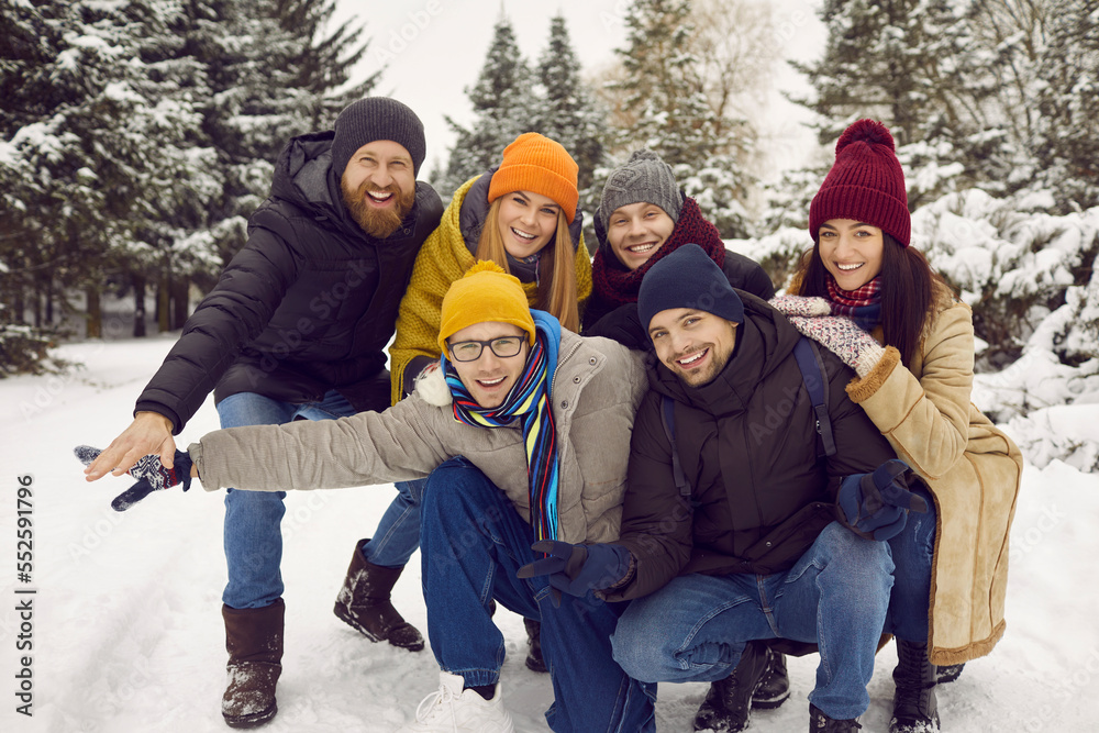 Portrait of overjoyed multiracial friends in outerwear have fun walk rest together in snowy forest. Smiling diverse multiethnic young people relax spend winter holidays or vacation outdoors.