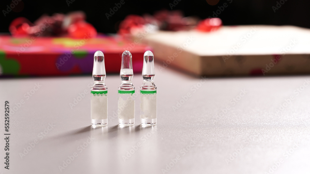 Glass ampoules with vaccine on a light gray background. Medicines on the background of gift boxes with bows Glass ampoules with vaccine on a light gray background. Medicines on the background of gift boxes with bows