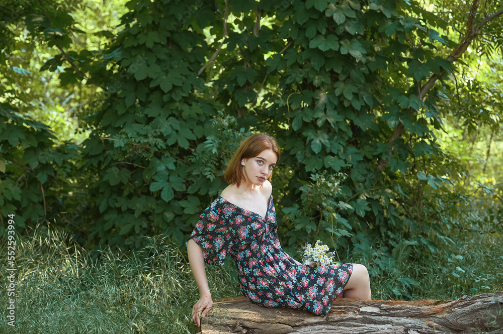 A young beautiful girl in a summer park enjoys a summer day sitting on a tree.