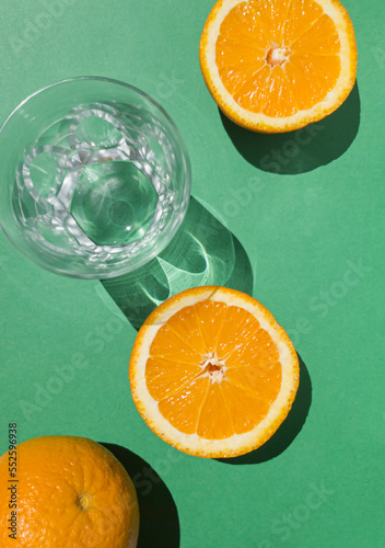 Composition with sliced orange fruit and empty glass on green background. Tropical summer minimal concept sunlit with sharp shadows