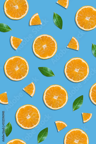 Summer flat lay pattern made with fresh orange fruit slices and green leaves on vibrant blue background. Minimal sunlight concept with sharp shadows.