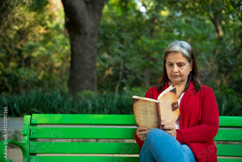 Indian senior woman reading book at park.