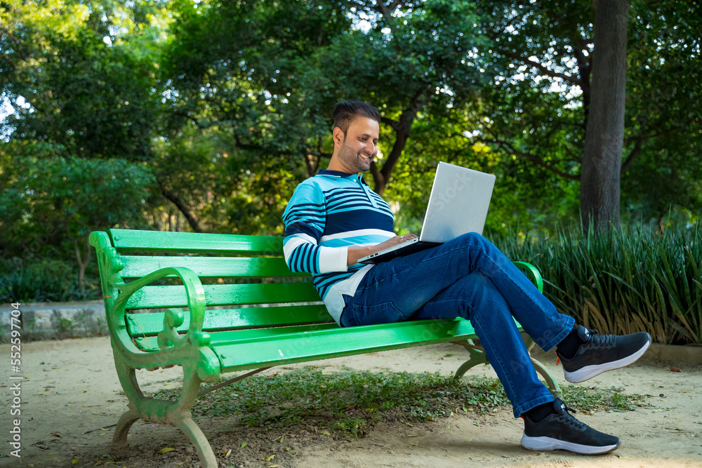 Young indian man working on laptop at park. Young indian man working on laptop at park.