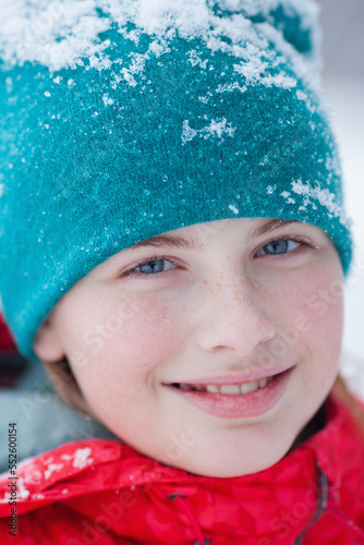 portrait of a blue-eyed teenage girl in a hat and winter clothes. Snowflakes on the cap and face