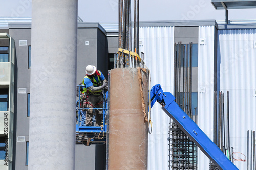 Workers on an aerial lift work on a concrete column at a construction site  photo