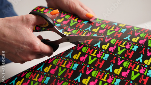 The process of wrapping a gift with women's hands for a birthday in colored gift paper with the inscription "happy birthday"