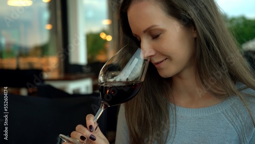 Woman drinking red wine from wine glass in restaurant or cafe. Expert tasting, smelling wine. photo